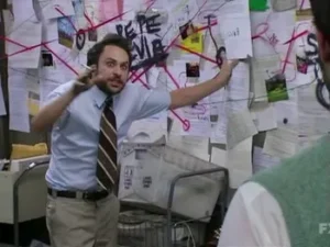 a screenshot from It's Always Sunny in Philadelphia, showing an agitated man standing in front of a wall covered in paper and red string